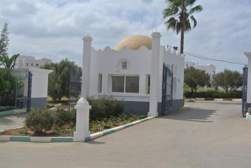 a white house with a gate and a palm tree at Appartement haut standing calme + piscines + WIFI in Asilah