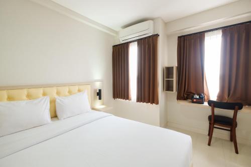 a bedroom with a large white bed and a chair at Cozy Studio with City View at Elvis Tower Apartment By Travelio in Cikarang