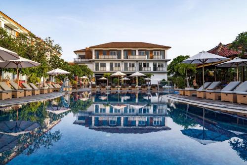 a hotel with a swimming pool with chairs and umbrellas at Kuta Beach Club Hotel in Kuta