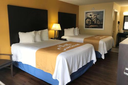 Days Inn by Wyndham Ridgeland South Carolina في ريدجلند: غرفة فندقية بسريرين وبطانيات بيضاء وبنية اللون