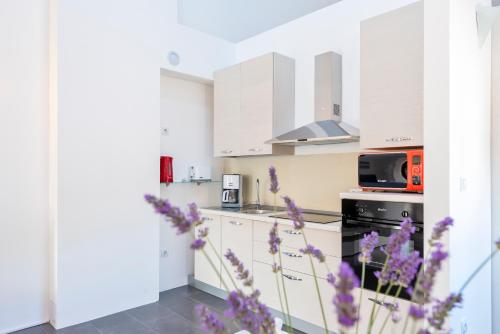 una cucina con armadi bianchi e fiori viola in primo piano di Lozna Residence a Postira (Postire)