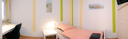 Habitación con cama con sábanas rosas y escritorio. en FineApartment Neumünster en Neumünster