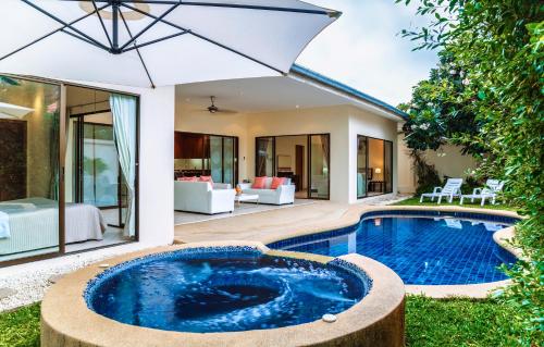 an outdoor pool with an umbrella next to a house at Magic Villas Pattaya in Pattaya South