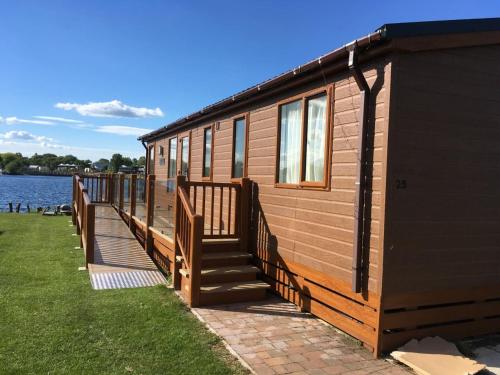 a large wooden cabin with stairs next to the water at Tattershall Lakeside Lodge Indulgent wheelchair accessible 8 berth with Hot Tub in Tattershall