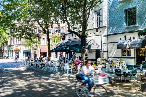 a man riding a bike down a street with tables and chairs at Alex Maastricht in Maastricht