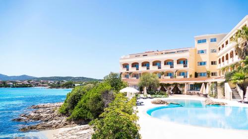 a hotel with a swimming pool next to a body of water at Gabbiano Azzurro Hotel & Suites in Golfo Aranci