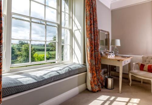 asiento junto a la ventana en una habitación con escritorio y ventana en Trewornan Manor, en Wadebridge