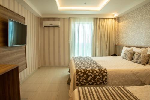 a hotel room with two beds and a flat screen tv at Paradiso Macae Hotel in Macaé