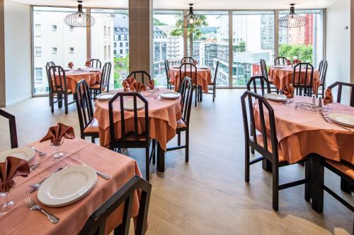 une salle à manger avec tables, chaises et fenêtres dans l'établissement Hôtel Acadia, à Lourdes