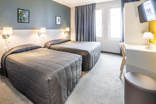 ルルドにあるHôtel Mirasolのベッド2台とデスクが備わるホテルルームです。