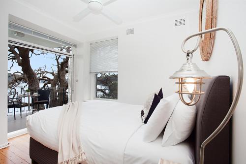 a white bedroom with a bed and a lamp at Serene And Stylish Harbourside Apartment in Sydney