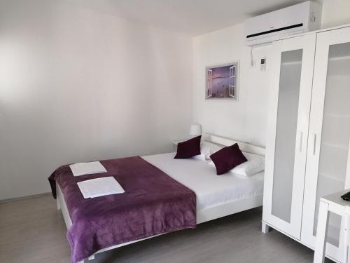 a white bedroom with a bed with purple sheets at Fjaka Camp in Pakoštane