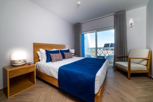 a bedroom with a bed and a chair and a window at AZUL in Zambujeira do Mar