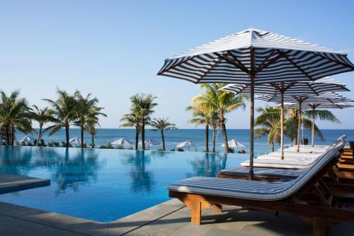 a pool with chairs and umbrellas next to the ocean at Cassia Cottage in Phu Quoc