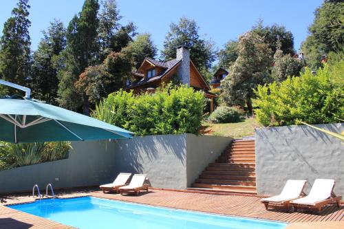 einem Pool mit Stühlen und einem Sonnenschirm neben einem Haus in der Unterkunft Cabañas Quetrihue in Villa La Angostura