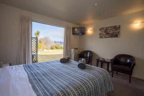 a bedroom with a bed with two chairs and a window at Loch Vista Bed & Breakfast in Te Anau