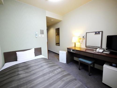 a hotel room with a bed and a desk with a mirror at Hotel Route-Inn Kamisuwa in Suwa