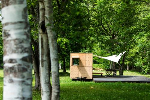 a small wooden structure in a park with trees at Snow Peak Jyubako（AKAIGAWA TOMO PLAYPARK） in Akaigawa