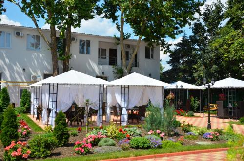 a garden in front of a white building with umbrellas at Vele Rosse Hotel, business & leisure in Odesa