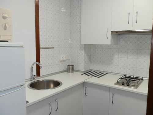 cocina blanca con fregadero y fogones en Apartamentos Turisticos Beatriz, en Perillo