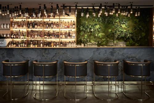 a bar with five bar stools in front of a shelf with bottles at Hotel Pacai, Vilnius, a Member of Design Hotels in Vilnius