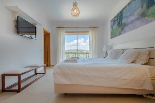 a white bedroom with a large bed and a window at Magnifica Moradia V4 in Casal da Lagoa Seca