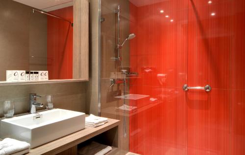 uma casa de banho com um lavatório e um chuveiro com paredes vermelhas em The Originals Boutique, Hôtel Les Strélitzias em Juan-les-Pins