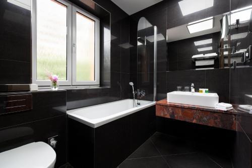 a black bathroom with a white tub and a sink at Hotel Selsky Dvur - Bohemian Village Courtyard in Prague