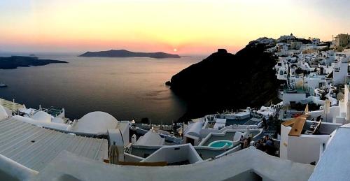 a sunset over a group of white buildings and the ocean at Aerino Villa in Firostefani