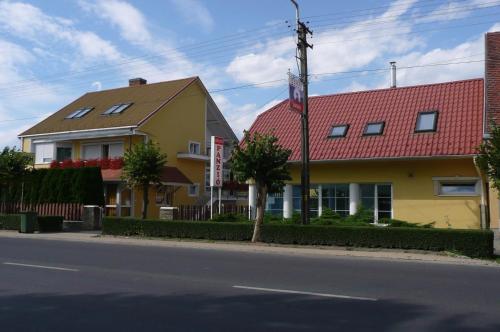 a yellow house with a red roof on a street at Szieszta Panzió in Sárvár