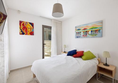 een witte slaapkamer met een bed en twee schilderijen aan de muur bij Lagoon Water Front Garden Patio in Herzliyya B