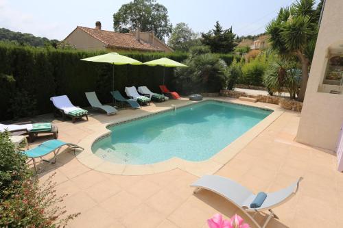 a swimming pool with chairs and umbrellas in a backyard at La Bastide des Pins in Le Pradet