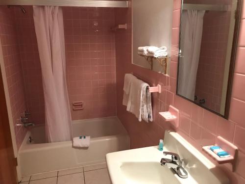 a pink bathroom with a sink and a bath tub at Simmons Motel and Suites in Hershey