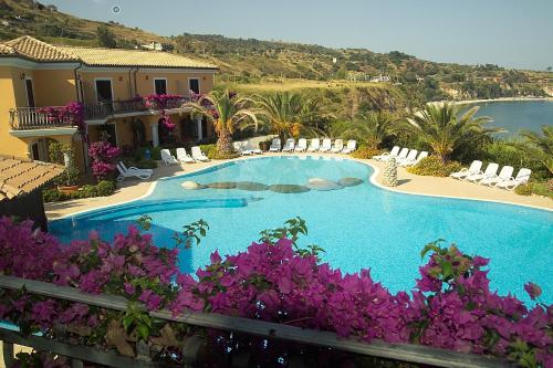 a swimming pool with purple flowers in front of a house at Villaggio Hotel Lido San Giuseppe in Briatico