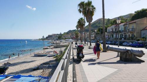 a woman walking down a sidewalk next to a beach at Three Rooms in Messina
