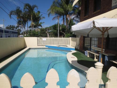 a swimming pool with a white umbrella next to a building at Aspley Pioneer Motel in Brisbane