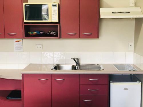 a kitchen with red cabinets and a sink and a microwave at Best Western Wellington in Wellington