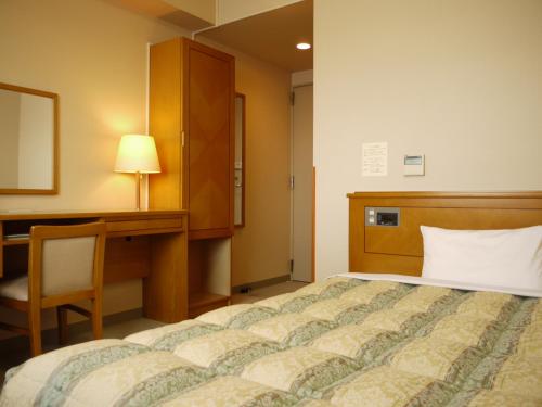 - une chambre avec un lit, un bureau et une lampe dans l'établissement Hotel Route-Inn Jouetsu, à Joetsu