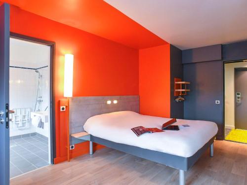a bed in a room with an orange wall at ibis budget Coutances in Coutances
