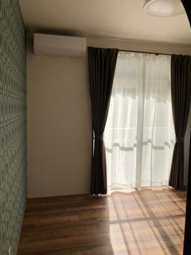 a room with a window with curtains and a wooden floor at Amami Weekly House Nico Nico Nazeko-ten in Amami
