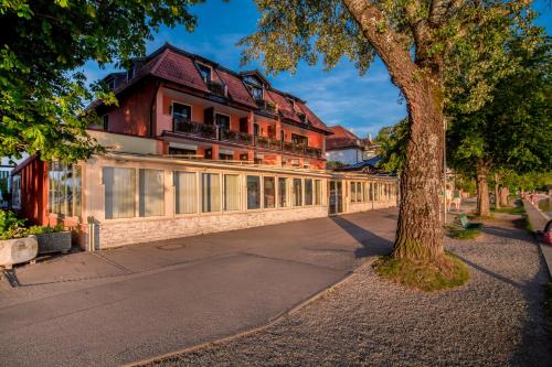 a building with a tree next to a street at Seehotel Pegasus in Herrsching am Ammersee