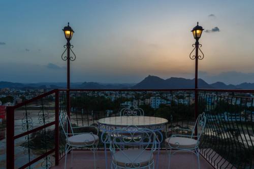 a table and chairs on a balcony with the sunset at Hotel Mewari Villa PURE VEG in Udaipur