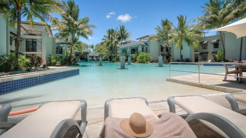 a person with a hat sitting on chairs in front of a swimming pool at Luxury Apartments at Temple Resort and Spa Port Douglas in Port Douglas
