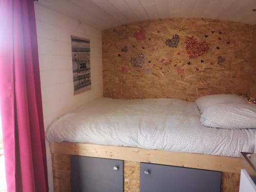 Una cama en una casa pequeña con una pared en Roulotte de la basse biguerie proche zoo de la flèche en Saint-Jean-de-la-Motte