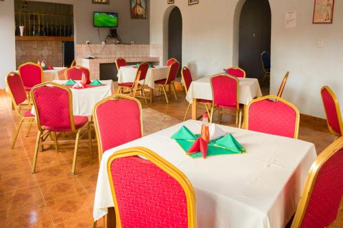 a dining room with white tables and red chairs at Palm Hotel in Mbale