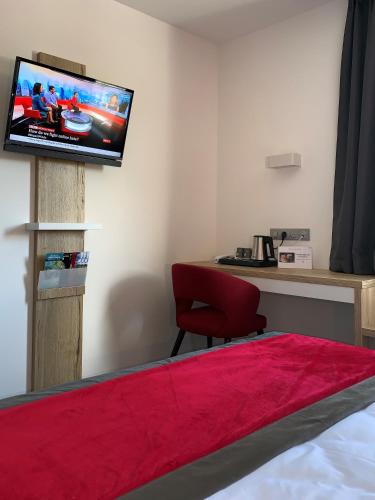 a room with a tv and a desk with a red chair at ATOLON PARK HOTEL in Brumath