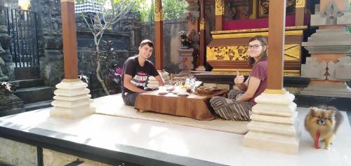 two women sitting at a table with a dog at SARI SEDANA HOME STAY in Gianyar