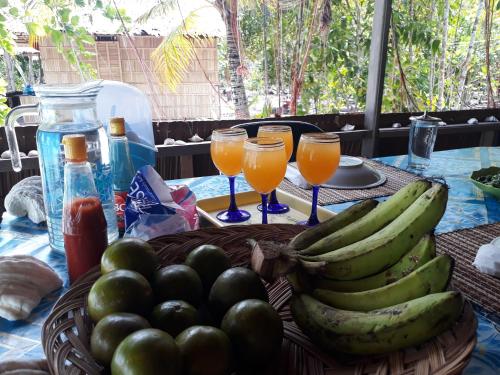 Turtle Dive Homestay في Kri: طاولة مع سلة من الفواكه وكؤوس من عصير البرتقال