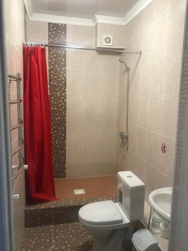uma casa de banho com um WC e um chuveiro com uma cortina de chuveiro vermelha. em Hotel Barhat Аktobe em Aqtöbe