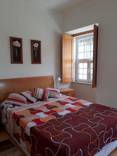 a bedroom with a bed with a colorful comforter and a window at Casa do Pelourinho in Vouzela